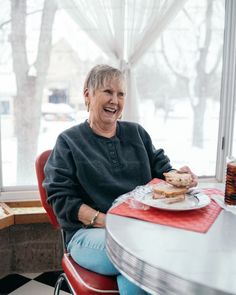 an older woman sitting at a table with food in front of her and smiling for the camera