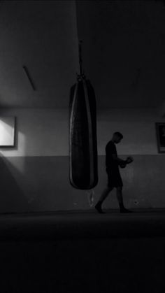 a man walking past a punching bag in a dark room with light coming through the window