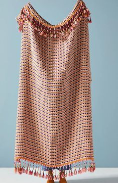 an orange and white blanket with tassels on it's edges, sitting on a table