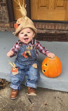 a toddler wearing overalls and a hat holding a pumpkin