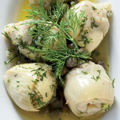 a white bowl filled with chicken covered in sauce and garnished with fresh herbs