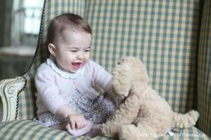 a baby sitting on a chair with a teddy bear in it's lap and smiling