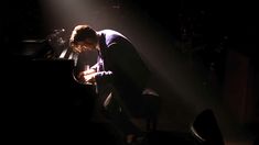 a man kneeling down in front of a piano with his hand on the keyboard and light coming from behind him