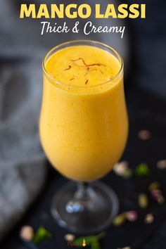 mango lassi thick and creamy in a glass on a black surface with text overlay