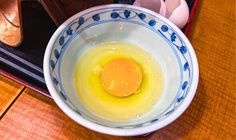 an egg yolk in a blue and white bowl on a wooden table next to some eggs