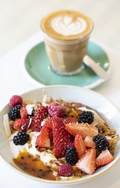 a bowl of fruit and yogurt with a cappuccino in the background