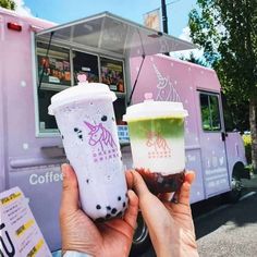 two people holding up cups in front of a food truck with unicorns on it