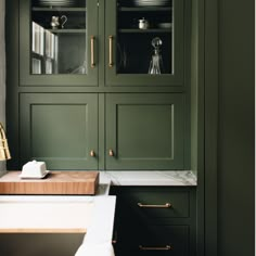 a kitchen with green cabinetry and marble counter tops, gold pulls on the handles