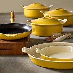 yellow pots and pans are lined up on a table with utensils in front of them