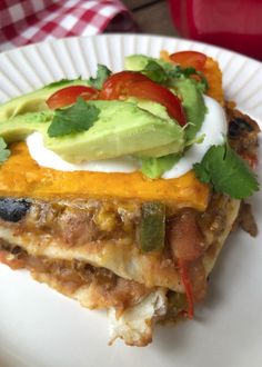 a piece of enchilada on a plate with avocado and tomatoes