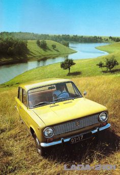 an old yellow car is parked on the side of a hill in front of a lake