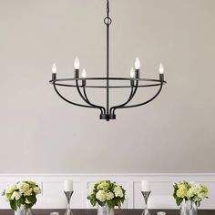 a chandelier hanging over a dining room table with vases and flowers on it