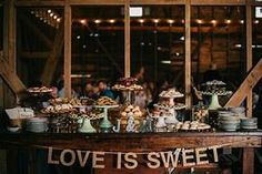 a wooden table topped with lots of desserts and pastries next to a sign that says love is sweet