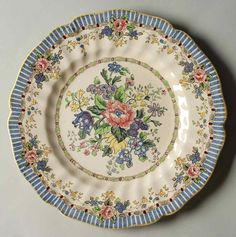 a plate with flowers painted on it and blue stripes around the edge, sitting on a white surface