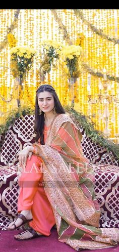 a woman sitting on top of a couch wearing an orange and green sari dress