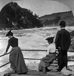 three people standing on a bridge looking at the water