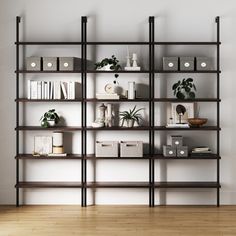 a book shelf with many books and plants on it in an empty room next to a white wall