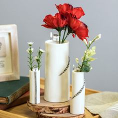 three white vases with red flowers in them on a wooden table next to an old book