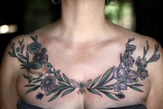 a woman's chest with purple flowers and leaves on her chest, in front of a dark background