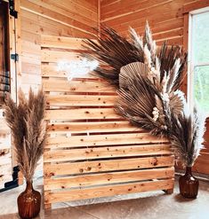 two vases filled with dried plants next to a wooden wall