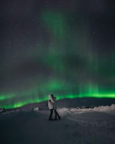 two people are standing in the snow under an auroral sky with green and red lights