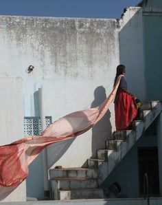 a woman is walking up some stairs with a long red scarf on her back and another person in the background