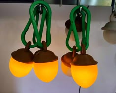 three green and yellow lights hanging from hooks on a white wall with a light fixture in the background