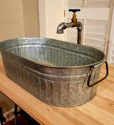 a metal tub sitting on top of a wooden table next to a faucet