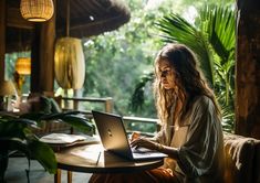 a woman sitting at a table with a laptop computer in front of her, while looking out the window