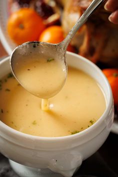 a spoon is being used to dip into a bowl of soup with oranges in the background