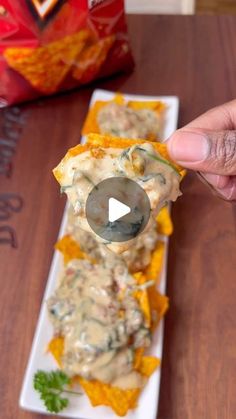 a person is holding a spoon over some food on a white plate with tortilla chips