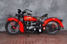 an orange and black motorcycle parked on top of a red brick floor next to a gray wall