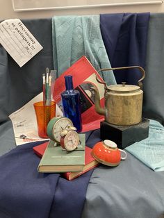 an assortment of books and other items sitting on a blue chair next to a tea kettle