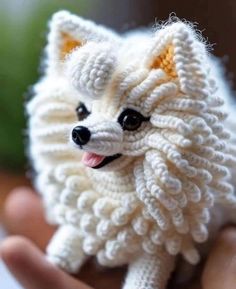 a hand holding a small white dog made out of knitted yarn with black eyes