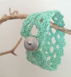 a green crochet bag hanging from a tree branch with a button on it