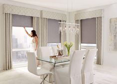 a woman standing in front of a dining room table with chairs and a chandelier