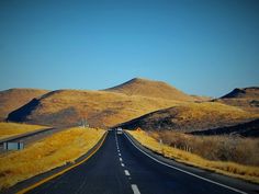 an empty road in the middle of nowhere with yellow grass and hills on either side