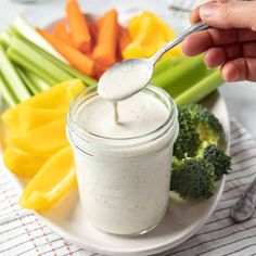 a person spooning dressing into a jar with vegetables and broccoli on the side