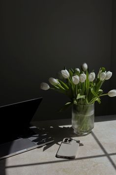 white tulips are in a glass vase next to a laptop