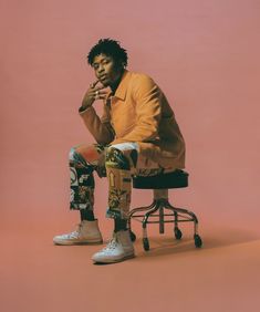 a man sitting on top of a chair next to a skateboard in front of a pink wall