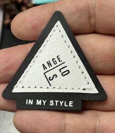 a hand holding a black and white triangle shaped pin with the word angle in my style on it