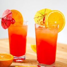 two glasses filled with orange juice and garnished with an umbrella next to sliced oranges