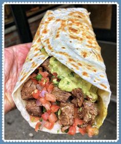 a burrito filled with meat, guacamole and tomatoes on top of it