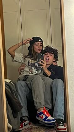 two people sitting on a bed taking a selfie in front of a mirror with one person holding a cell phone