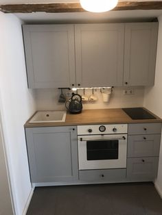 a kitchen with an oven, sink and kettle on the counter top in front of white cupboards