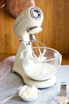 an electric mixer with whipped cream in it on top of a counter next to other ingredients