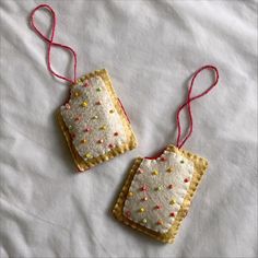 two handmade christmas ornaments hanging on a white sheet with red twine and thread