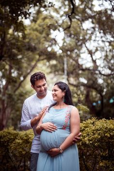 a man and woman standing next to each other in front of trees with their hands on the pregnant belly