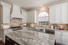 a large kitchen with marble counter tops and white cabinets, along with an arched window