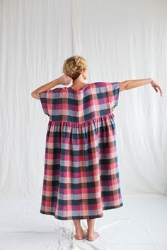 a woman standing in front of a white backdrop wearing a pink and blue checkered dress